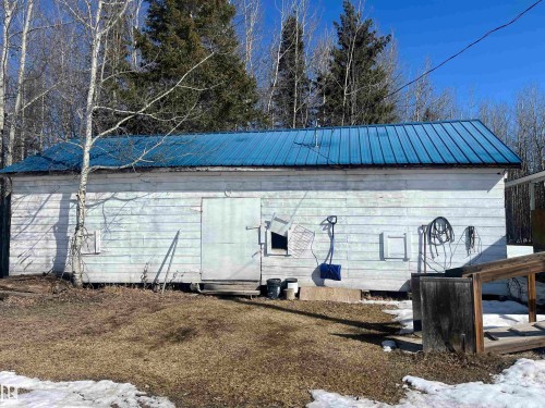 The property features an exterior building with white siding and a blue metal roof, set against a backdrop of trees - 55131 Range Road 83, Rural Yellowhead, AB - Outdoor
