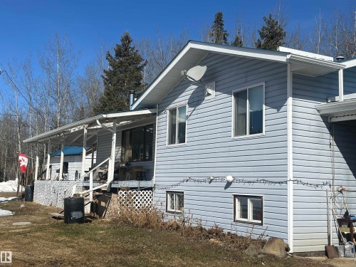 The property features light blue siding, multiple windows, and a covered porch area with white lattice detailing - 55131 Range Road 83, Rural Yellowhead, AB - Outdoor