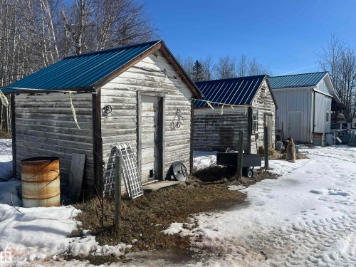 The property includes several outbuildings with metal roofs, set against a backdrop of bare trees and clear skies - 55131 Range Road 83, Rural Yellowhead, AB - Outdoor
