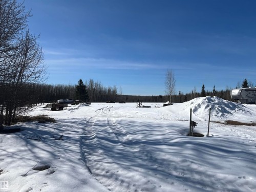 The property features an expansive, snow-covered open area, bordered by a dense line of trees in the distance - 55131 Range Road 83, Rural Yellowhead, AB - Outdoor With View