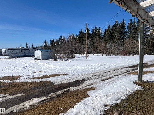 The property features a spacious outdoor area with areas of snow cover, a detached shed, and mature evergreen trees in the background - 55131 Range Road 83, Rural Yellowhead, AB - Outdoor