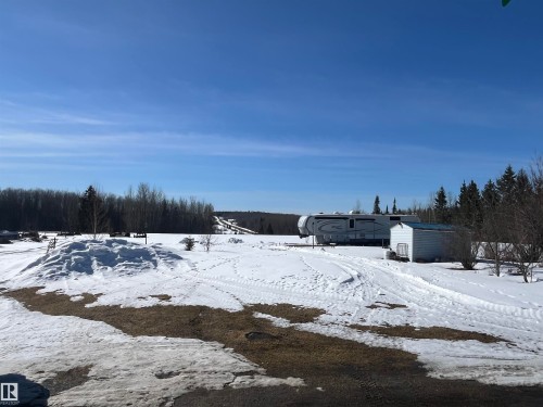 The property includes a substantial snow-covered area with visible ground patches, bordered by a dense line of evergreen trees - 55131 Range Road 83, Rural Yellowhead, AB - Outdoor