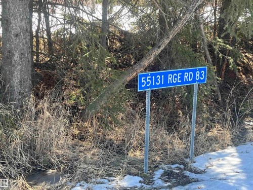 The property is identified by a prominent blue street sign, set against a backdrop of mature trees and natural vegetation - 55131 Range Road 83, Rural Yellowhead, AB - Outdoor