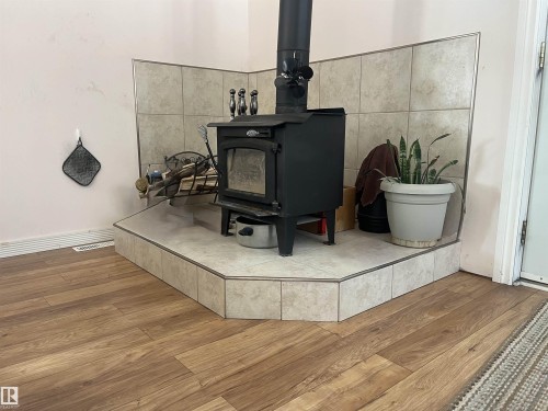 The property features a corner wood-burning stove with a tiled hearth and wall surround, complemented by wood-look flooring - 55131 Range Road 83, Rural Yellowhead, AB - Indoor