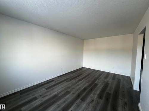 The room features dark wood-look flooring and white walls, creating a clean and versatile aesthetic - 3323 107 Avenue Nw, Edmonton, AB - Indoor Photo Showing Other Room