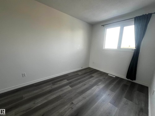 Room featuring light-colored walls, dark-toned flooring, and a window with a dark curtain - 3323 107 Avenue Nw, Edmonton, AB - Indoor Photo Showing Other Room
