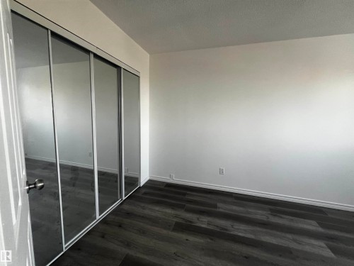This room features dark wood-look flooring and a closet with mirrored sliding doors - 3323 107 Avenue Nw, Edmonton, AB - Indoor Photo Showing Other Room