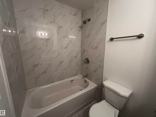 Bathroom featuring a bathtub with a shower, white tiled walls with a grey veining pattern, and a toilet - 3323 107 Avenue Nw, Edmonton, AB - Indoor Photo Showing Bathroom