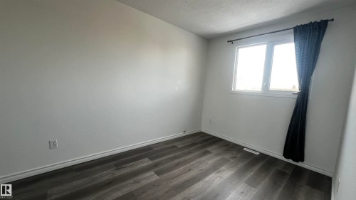 This room features light-colored walls, dark wood-style flooring, and a window with a curtain rod - 3323 107 Avenue Nw, Edmonton, AB - Indoor Photo Showing Other Room