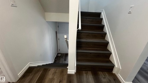 Staircase featuring dark wood-look treads and risers, white handrails, and light grey walls - 3323 107 Avenue Nw, Edmonton, AB - Indoor Photo Showing Other Room