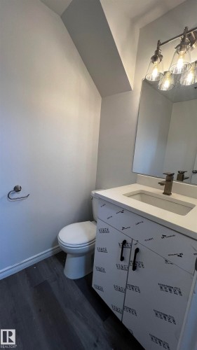 This bathroom features a vanity with a white countertop and a contemporary light fixture - 3323 107 Avenue Nw, Edmonton, AB - Indoor Photo Showing Bathroom