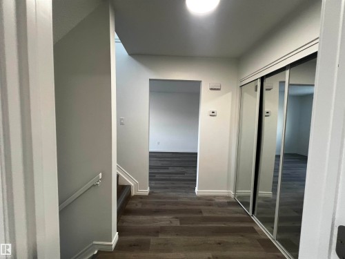 Entryway featuring wood-look flooring, a closet with mirrored sliding doors, and a staircase with a handrail - 3323 107 Avenue Nw, Edmonton, AB - Indoor Photo Showing Other Room