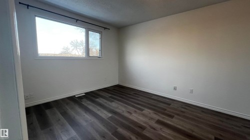 This room features dark wood-look flooring and white walls, creating a clean and versatile aesthetic - 3323 107 Avenue Nw, Edmonton, AB - Indoor Photo Showing Other Room