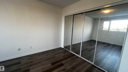 This room features dark wood-style flooring, white walls, and a closet with mirrored sliding doors - 3323 107 Avenue Nw, Edmonton, AB - Indoor Photo Showing Other Room