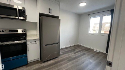 This property features a kitchen area with stainless steel appliances, including a microwave, oven, and refrigerator, complemented by white cabinetry and light-colored countertops - 3323 107 Avenue Nw, Edmonton, AB - Indoor Photo Showing Kitchen