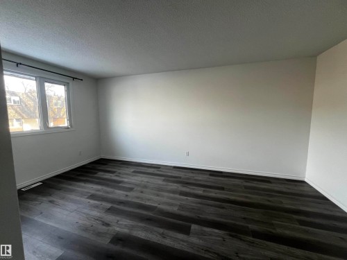 This room features dark-toned flooring, white walls, and a window with a view of exterior structures - 3323 107 Avenue Nw, Edmonton, AB - Indoor Photo Showing Other Room