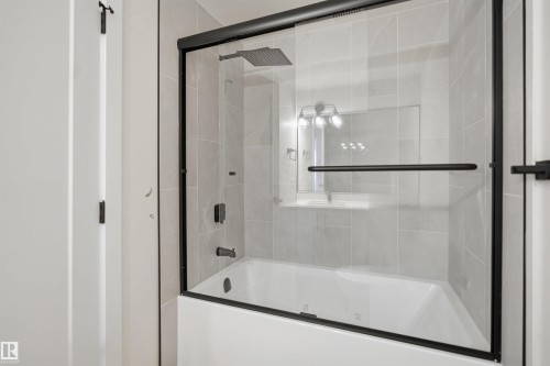 Bathroom featuring a bathtub with a clear glass enclosure and matte black trim - 1706 37 Street, Edmonton, AB - Indoor Photo Showing Bathroom