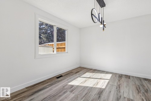 Bright room featuring a window overlooking mature trees and a wooden fence, light-toned flooring, and a modern ceiling light fixture - 95 Ridgewood Terrace, St. Albert, AB - Indoor Photo Showing Other Room