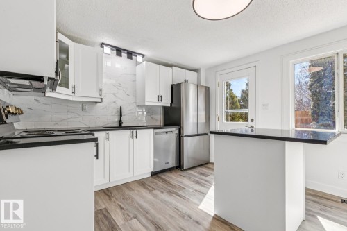 The kitchen features white cabinetry, black countertops, a stainless steel refrigerator, and a door leading to the exterior - 95 Ridgewood Terrace, St. Albert, AB - Indoor Photo Showing Kitchen With Stainless Steel Kitchen With Upgraded Kitchen