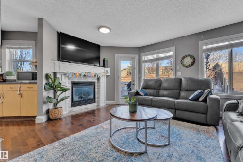 Spacious living area featuring hardwood flooring, a fireplace with a white mantel, and large windows providing ample natural light - 3609 11 Street, Edmonton, AB - Indoor Photo Showing Living Room With Fireplace