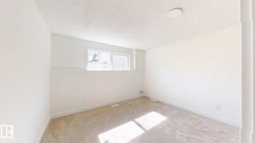 This room features neutral-toned carpet, a window providing natural light, and a ceiling light fixture - 8515 86 Avenue, Edmonton, AB 