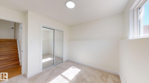 This room features light-colored carpet, a window, and a mirrored sliding closet door - 8515 86 Avenue, Edmonton, AB 