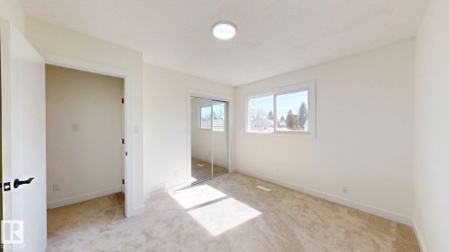 A bright room with carpeted flooring, a window offering views of trees, and a mirrored sliding closet door - 8515 86 Avenue, Edmonton, AB 