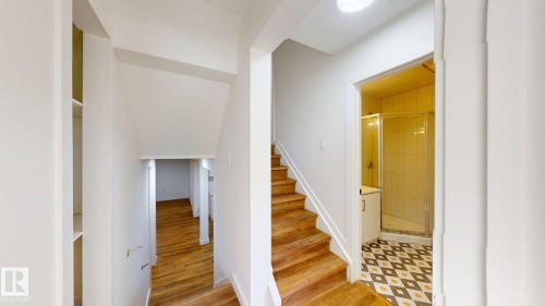 This property features hardwood stairs, a hallway with hardwood flooring, and a bathroom with patterned floor tiles and a shower enclosure - 8515 86 Avenue, Edmonton, AB 