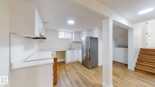 This property features a kitchen area with white cabinetry, a stainless steel refrigerator, and wood-look flooring - 8515 86 Avenue, Edmonton, AB 
