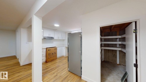 The kitchen area features white cabinetry, an exhaust hood, and wood-look flooring - 8515 86 Avenue, Edmonton, AB 