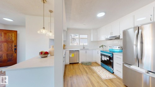 The kitchen features white cabinetry, stainless steel appliances, and light wood-tone flooring - 8515 86 Avenue, Edmonton, AB 
