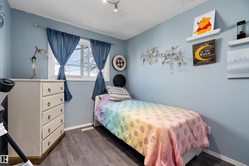 This room features a window with blue curtains, light blue walls, and dark flooring - 28 Camelot Avenue, Leduc, AB - Indoor Photo Showing Bedroom