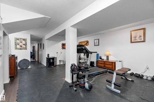 The property features a versatile area with white walls and a combination of dark wood flooring and dark rubber mat flooring - 28 Camelot Avenue, Leduc, AB - Indoor Photo Showing Gym Room