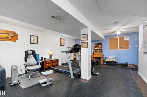 This versatile room features white and blue painted walls, ceiling beams, and a ceiling fan - 28 Camelot Avenue, Leduc, AB - Indoor Photo Showing Gym Room