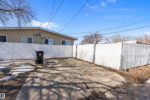 The property features a concrete paved area, enclosed by white chain-link fencing, and a stucco exterior on the visible side of the building - 28 Camelot Avenue, Leduc, AB - Outdoor