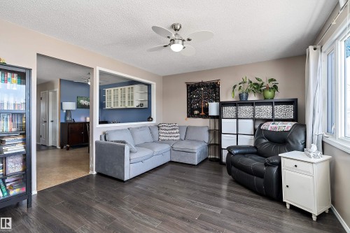 The living area features dark wood-style flooring, a ceiling fan with lighting, and a large window providing natural light - 28 Camelot Avenue, Leduc, AB - Indoor Photo Showing Living Room