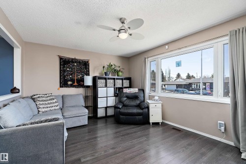 The living area features dark wood-style flooring, a ceiling fan with integrated lighting, and a large window providing natural light - 28 Camelot Avenue, Leduc, AB - Indoor Photo Showing Living Room