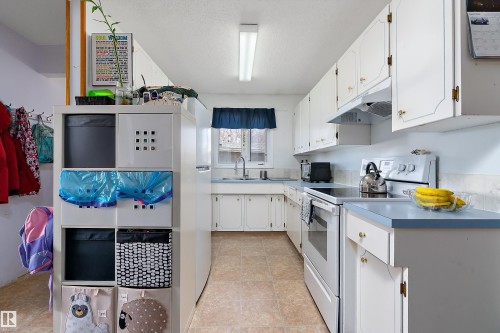 The kitchen features white cabinetry with gold-toned hardware, light blue countertops, and white appliances including an oven with a stovetop - 28 Camelot Avenue, Leduc, AB - Indoor Photo Showing Kitchen With Double Sink