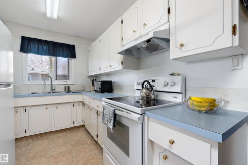 The kitchen features white cabinetry with gold hardware, blue countertops, and a white oven with an overhead exhaust fan - 28 Camelot Avenue, Leduc, AB - Indoor Photo Showing Kitchen With Double Sink