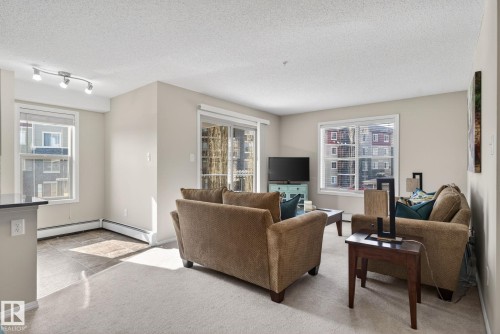 The living area features a glass sliding door, two windows with blinds, light-colored walls, and a combination of carpet and tiled flooring - 215 1080 Mcconachie Boulevard, Edmonton, AB - Indoor Photo Showing Living Room