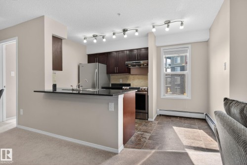 The property features a kitchen with dark cabinetry, stainless steel appliances, and a dark countertop - 215 1080 Mcconachie Boulevard, Edmonton, AB - Indoor Photo Showing Kitchen With Stainless Steel Kitchen