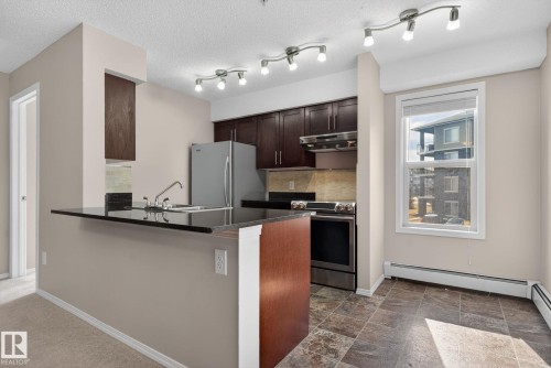 The kitchen features dark wood cabinetry, a stainless steel refrigerator, and a stainless steel oven with an overhead microwave - 215 1080 Mcconachie Boulevard, Edmonton, AB - Indoor Photo Showing Kitchen With Stainless Steel Kitchen