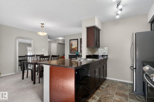The property features an open concept kitchen and dining area with dark wood cabinetry, granite countertops, and a tiled floor in the kitchen - 215 1080 Mcconachie Boulevard, Edmonton, AB - Indoor Photo Showing Kitchen With Double Sink