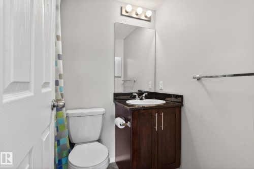 The bathroom features a vanity with a dark wood cabinet and a countertop with an integrated sink, a mirror, and overhead lighting - 215 1080 Mcconachie Boulevard, Edmonton, AB - Indoor Photo Showing Bathroom