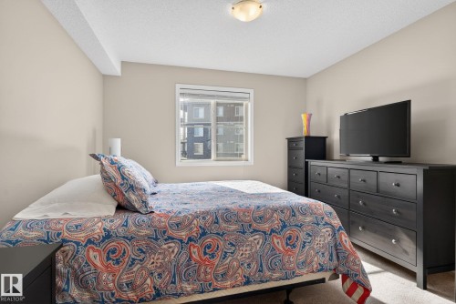 Bedroom featuring light beige walls, a window with a view of exterior buildings, and carpeted flooring - 215 1080 Mcconachie Boulevard, Edmonton, AB - Indoor Photo Showing Bedroom