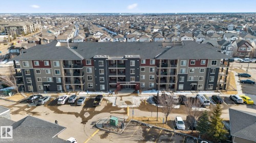 The property features a multi-story building with a dark grey roof and a facade with grey and reddish-brown accents - 215 1080 Mcconachie Boulevard, Edmonton, AB - Outdoor