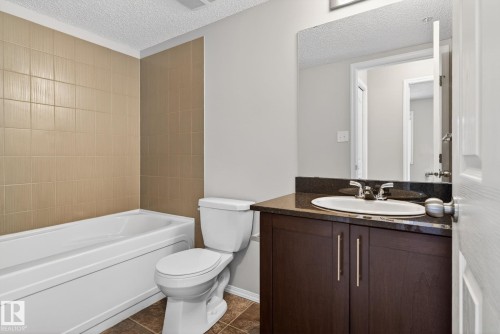 Bathroom featuring a white bathtub, a tiled shower surround, a white toilet, and a vanity with an integrated sink and mirror - 215 1080 Mcconachie Boulevard, Edmonton, AB - Indoor Photo Showing Bathroom