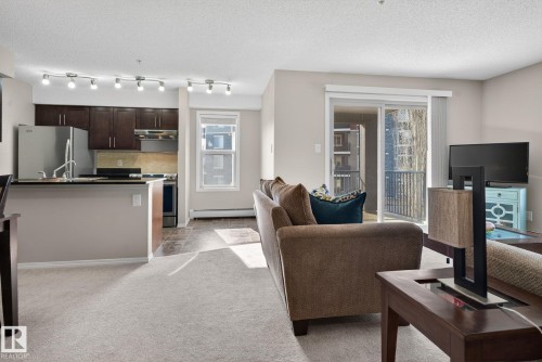 Spacious living area featuring light-colored carpeting and a sliding glass door that opens to a balcony - 215 1080 Mcconachie Boulevard, Edmonton, AB - Indoor