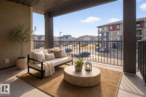 The property features a private balcony with a durable concrete floor, an outdoor rug, and a black metal railing - 215 1080 Mcconachie Boulevard, Edmonton, AB - Outdoor With Balcony With Exterior