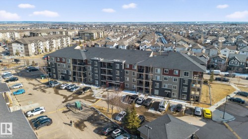 The property features a multi-story building with a dark roof and balconies, surrounded by paved parking areas - 215 1080 Mcconachie Boulevard, Edmonton, AB - Outdoor With View